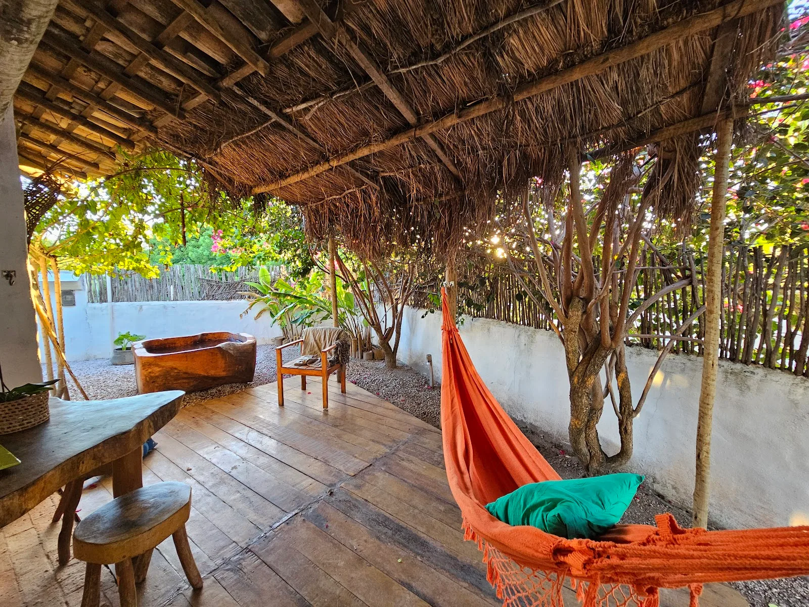 Terraço de madeira com rede laranja e mesa, aberto para o jardim do Pontal da Enseada