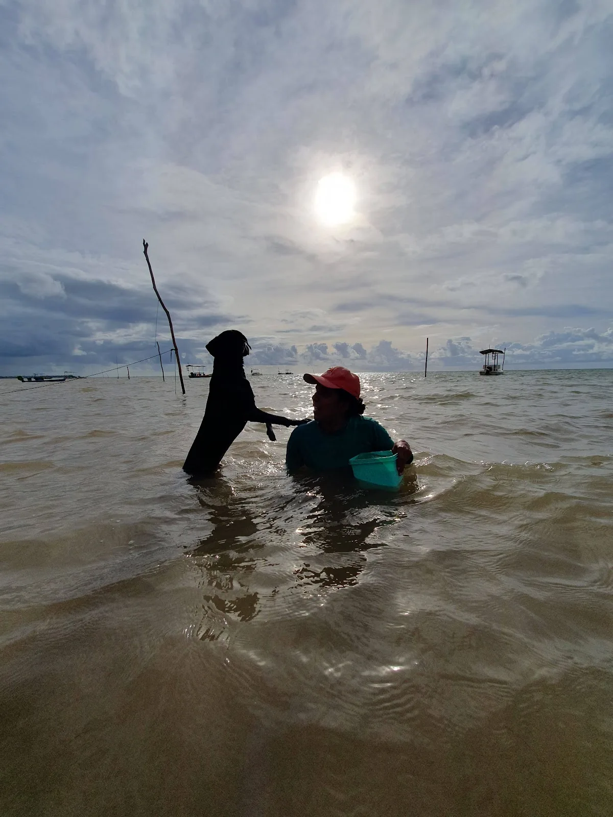 Duas pessoas pescando na água rasa, sob um sol coberto por nuvens, em Tatuamunha