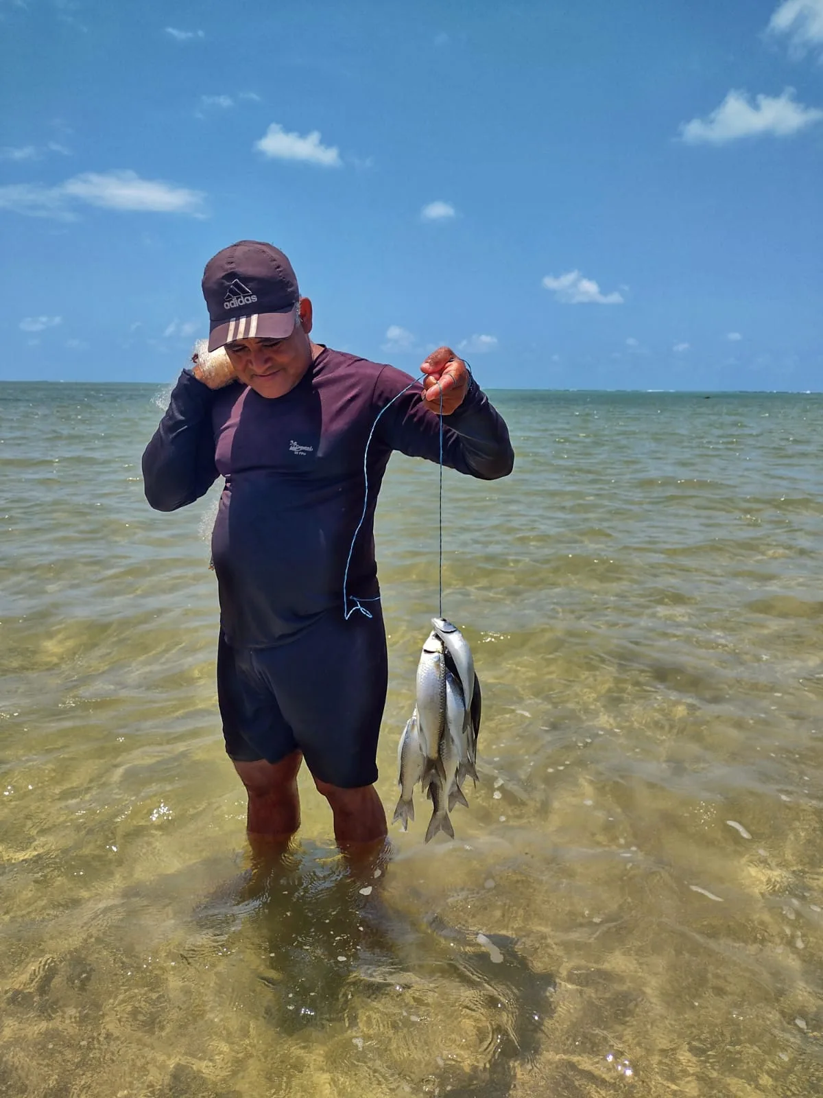 Pescador com água até a cintura, segurando um peixe, no mar de Tatuamunha