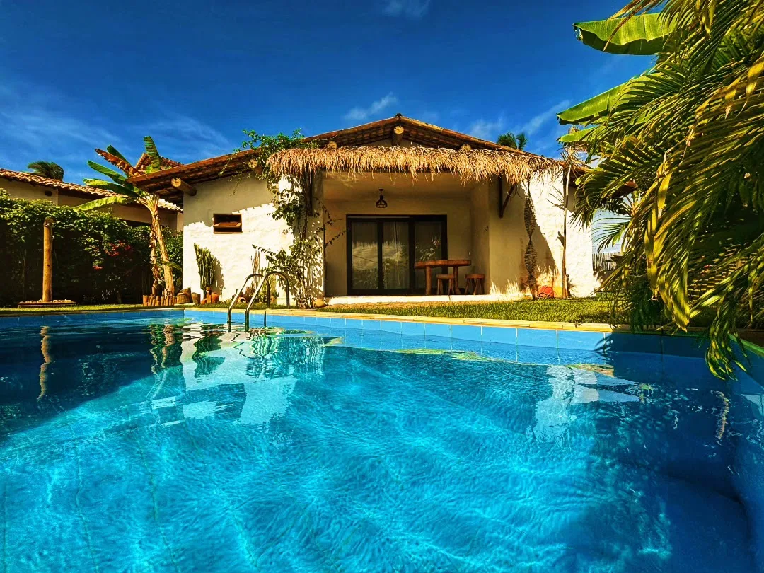 Piscina e casa de telhado de palha do Pontal da Enseada, cercadas de vegetação