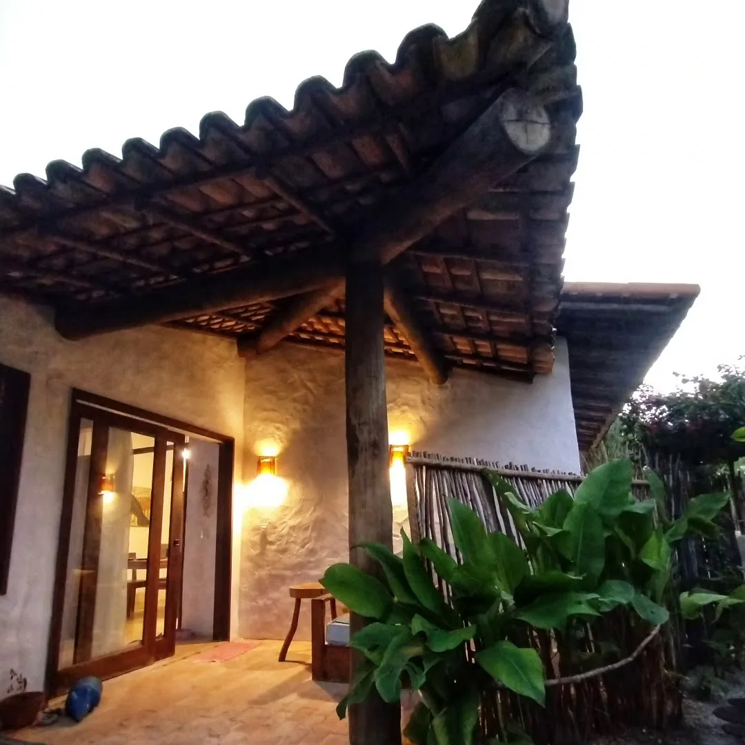 Varanda de uma das casas do Pontal da Enseada, com telhado de madeira e plantas