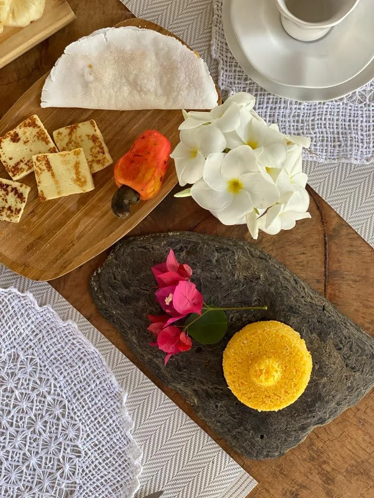 Tábua com queijos, frutas e flores sobre uma mesa de madeira